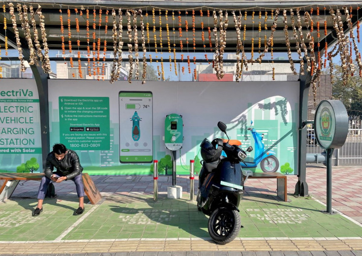 A man checks his mobile phone as he waits while recharging his Ola electric scooter at an electric vehicle charging station in New Delhi, India, February 12, 2022. 