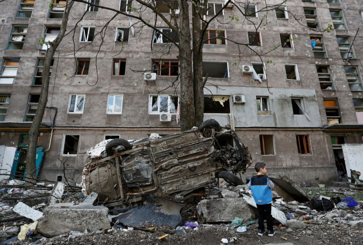 A boy stands next to a wrecked vehicle in front of an apartment building damaged during Ukraine-Russia conflict in the southern port city of Mariupol, Ukraine April 24, 2022. 