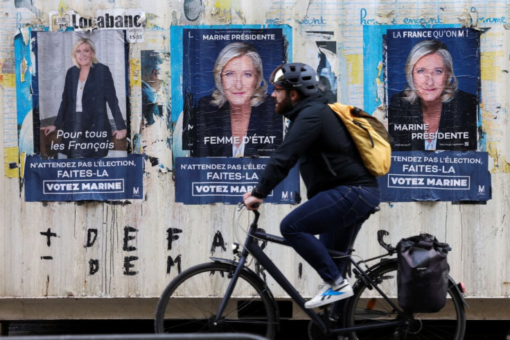A man rides a bike in front of posters of Marine Le Pen, French far-right National Rally (Rassemblement National) party candidate for the 2022 French presidential election outside the party headquarters, after her defeat in the second round of the electio