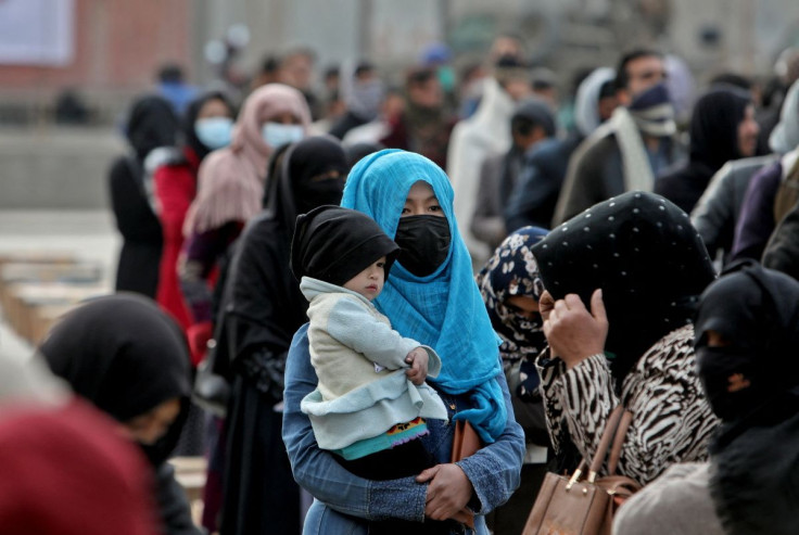An Afghan woman holds her child as she and others wait to receive package being distributed by a Turkish humanitarian aid group at a distribution centre in Kabul, Afghanistan, December 15, 2021.