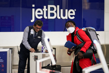 An unmasked JetBlue Airlines worker assists a masked traveler after the Biden administration announced it would no longer enforce a U.S. coronavirus disease (COVID-19) mask mandate on public transportation, following a federal judge's ruling that the 14-m