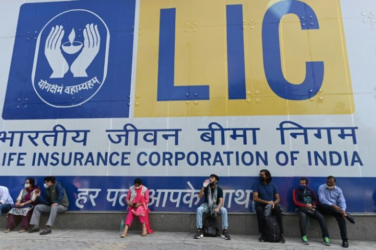 People sit by a promotional poster for Life Insurance Corporation in New Delhi