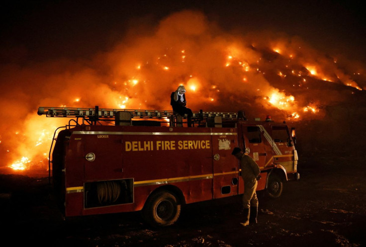 A firefighter uses his mobile phone as he sits on top of a fire truck as smoke billows from burning garbage at the Bhalswa landfill site in New Delhi, India, April 27, 2022.