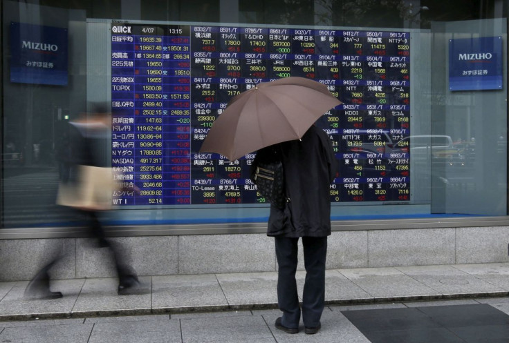 A man holding an umbrella looks at an electronic stock quotation board outside a brokerage in Tokyo April 7, 2015.  