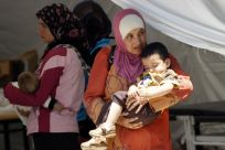 Syrian women wait for medical assistance for their children at a refugee camp in Yayladagi in Hatay province