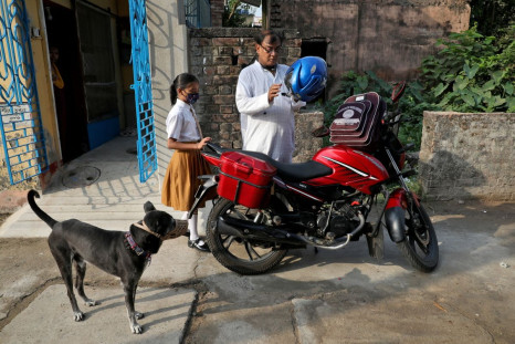 Ambika Chatterjee, 9, a student of fifth grade, who according to her father Subhasish Chatterjee, 52, shifted to a low fee charging private school from an elite school, waits for her father as he puts on his helmet to drop her to a school in Kolkata, Indi