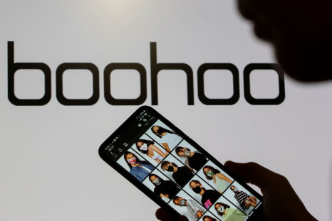 A woman poses with a smartphone showing the Boohoo app in front of the Boohoo logo on display in this illustration taken September 30, 2020. 