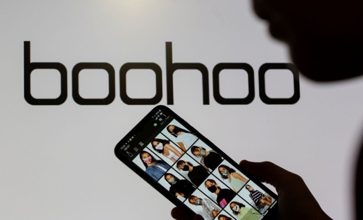 A woman poses with a smartphone showing the Boohoo app in front of the Boohoo logo on display in this illustration taken September 30, 2020. 