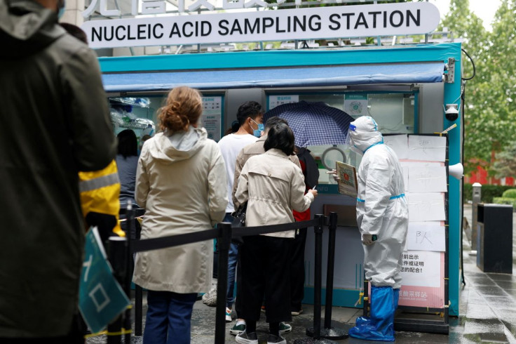 People line up to get tested next to a staff member wearing personal protective equipment (PPE) at a mobile nucleic acid testing site outside a shopping mall, amid the coronavirus disease (COVID-19) outbreak in Beijing, China May 6, 2022. 