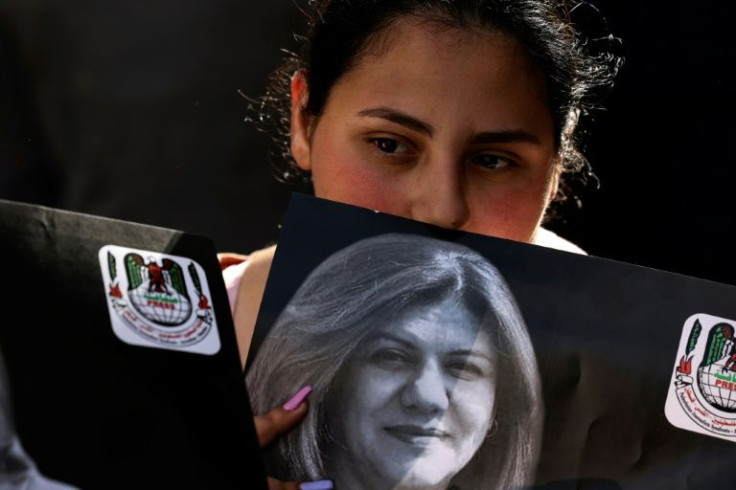 A Palestinian woman holds a photograph of slain veteran Al Jazeera journalist Shireen Abu Akleh, as her body is carried toward the offices of the news channel in the West Bank city of Ramallah, on May 11, 2022