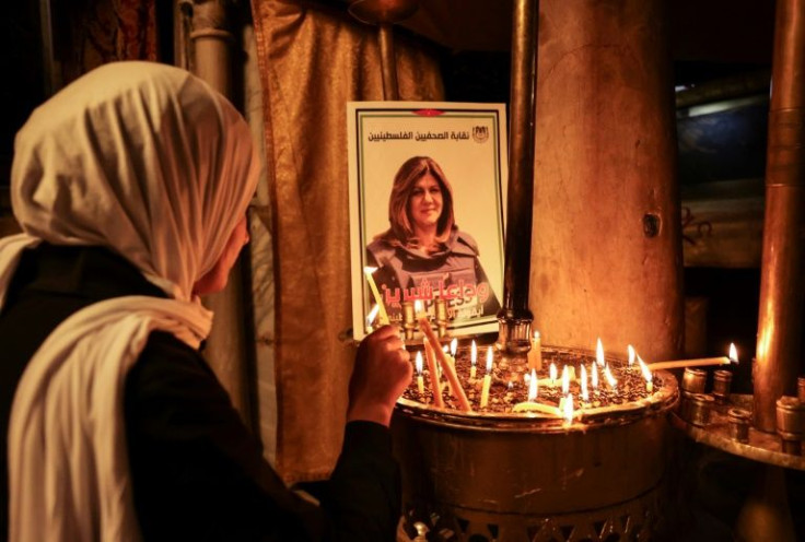 A woman lights a candle in front of a poster depicting veteran Al-Jazeera journalist Shireen Abu Akleh at the the Church of the Nativity in the West Bank biblical city of Bethlehem on May 11, 2022
