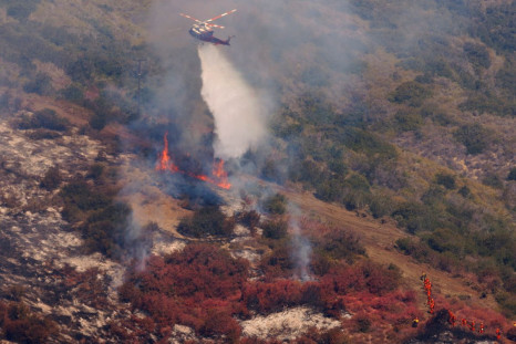 A helicopter drops water as it assists firefighters battling a hillside fire that burned through a neighborhood and destroyed homes in Laguna Niguel, California, U.S., May 12, 2022.    