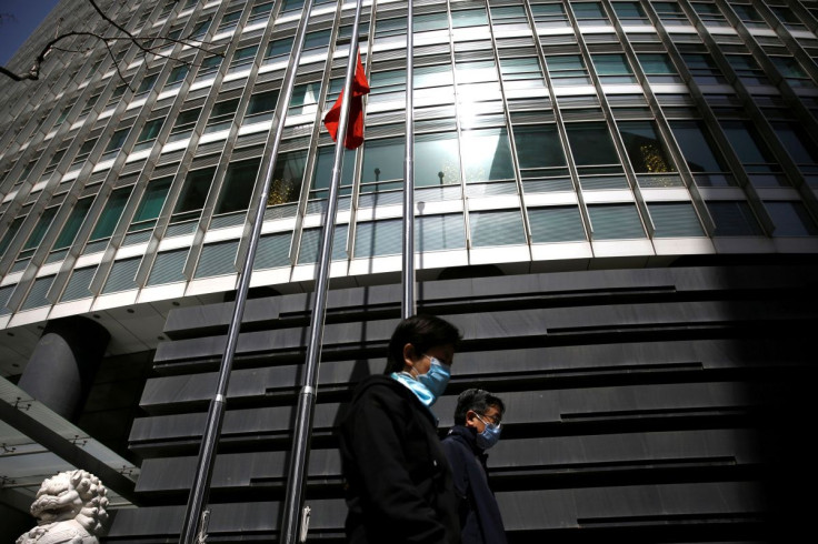 People wearing face masks walk past a bank, where the Chinese national flag flies at half-mast in Beijing as China holds a national mourning for those who died of the coronavirus disease (COVID-19), on the Qingming tomb-sweeping festival, April 4, 2020. 