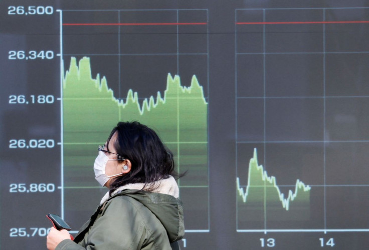 A passerby wearing a protective face mask walks past an electric screen displaying a graph showing Japan's Nikkei share average, amid the coronavirus disease (COVID-19) pandemic, in Tokyo, Japan February 24, 2022.  