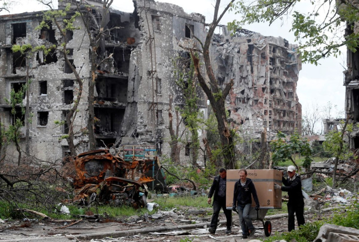 Local residents transport a box on a wheelbarrow past a heavily damaged apartment building near Azovstal Iron and Steel Works, during Ukraine-Russia conflict in the southern port city of Mariupol, Ukraine May 22, 2022. 