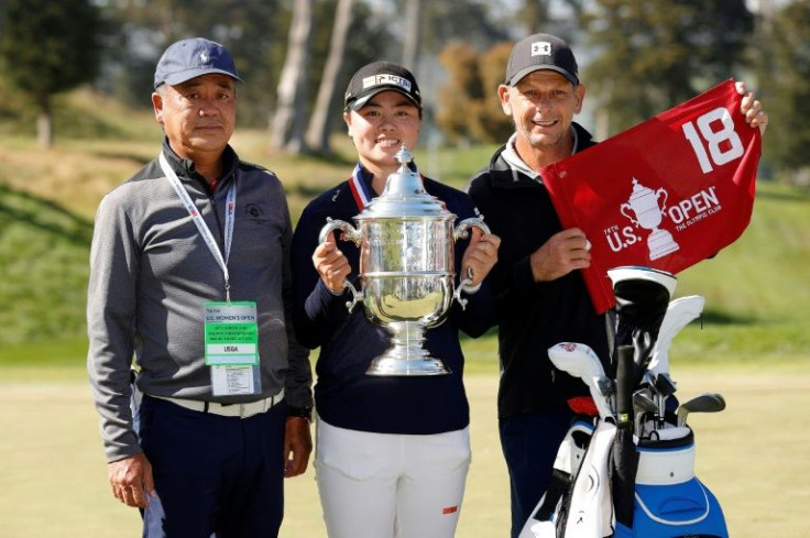 Yuka Saso lifts the US Open trophy a year ago flanked by father Masakazu Saso (left) and caddie Lionel Matichuk
