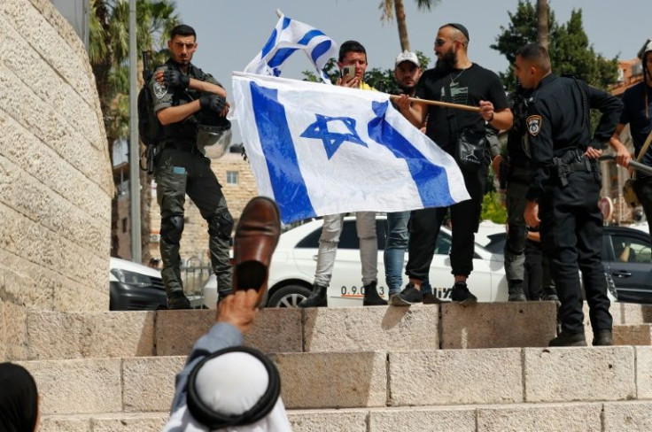 A Palestinian man in east Jerusalem raises a shoe against Israelis waving their national flags at Damascus Gate on May 29, 2022, ahead of the start of the 'flag march'