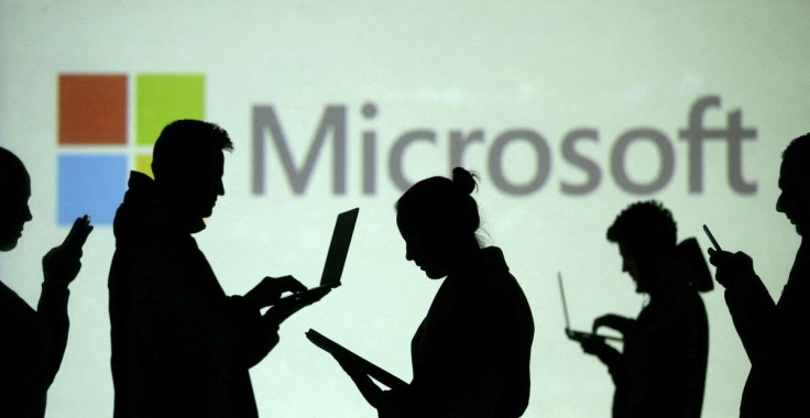 Silhouettes of laptop and mobile device users are seen next to a screen projection of Microsoft logo in this picture illustration taken March 28, 2018.  