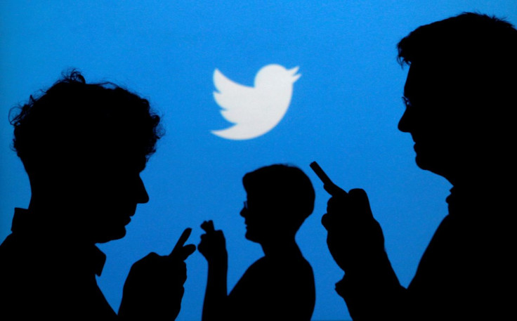 People holding mobile phones are silhouetted against a backdrop projected with the Twitter logo in this illustration picture taken September 27, 2013. 