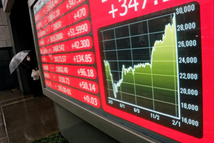 A woman holding an umbrella walks near an electric board showing Nikkei index at a brokerage in Tokyo, Japan February 15, 2021. 