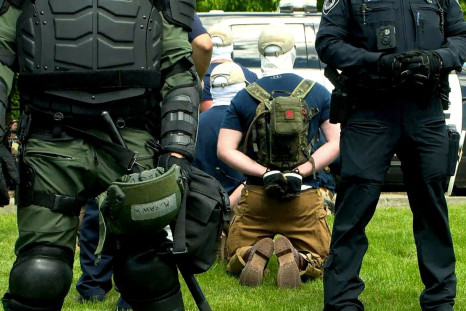 Police officers in riot gear guard a group of men, who police say are among 31 arrested for conspiracy to riot and are affiliated with the group Patriot Front, after they were found in the rear of a U Haul van in the vicinity of a Pride event in Coeur d'A
