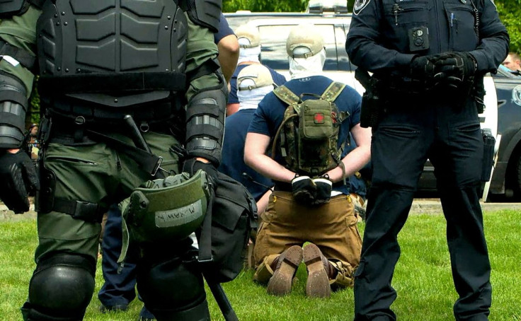 Police officers in riot gear guard a group of men, who police say are among 31 arrested for conspiracy to riot and are affiliated with the group Patriot Front, after they were found in the rear of a U Haul van in the vicinity of a Pride event in Coeur d'A