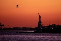 In this file photo taken on October 14, 2019 a helicopter flies past the Statue of Liberty as the sun sets in New York City