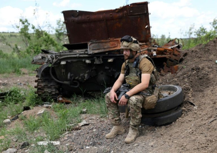 Seorang prajurit Ukraina duduk di sebelah tank Rusia yang hancur tidak jauh dari Lysychansk pada hari Jumat