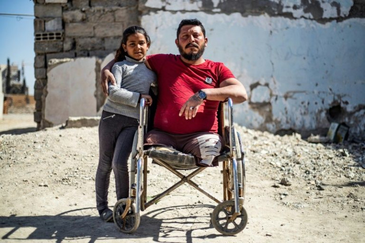 Ahmad Hajj Hmaidy, who lost his legs as a result of a landmine explosion, poses with his only surviving daughter Nada outside their destroyed family home in the Syrian city of Raqa in February 2021