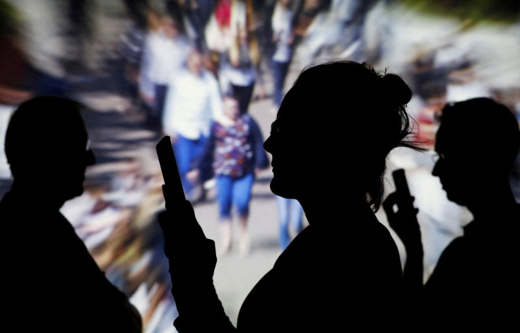 People look at data on their mobiles as background with crowd of people walking is projected in this illustration picture taken on May 30, 2018. 