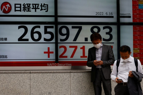 Men wearing protective masks amid the coronavirus disease (COVID-19) outbreak, use mobile phones in front of an electronic board displaying Japan's Nikkei index outside a brokerage in Tokyo, Japan June 16, 2022. 