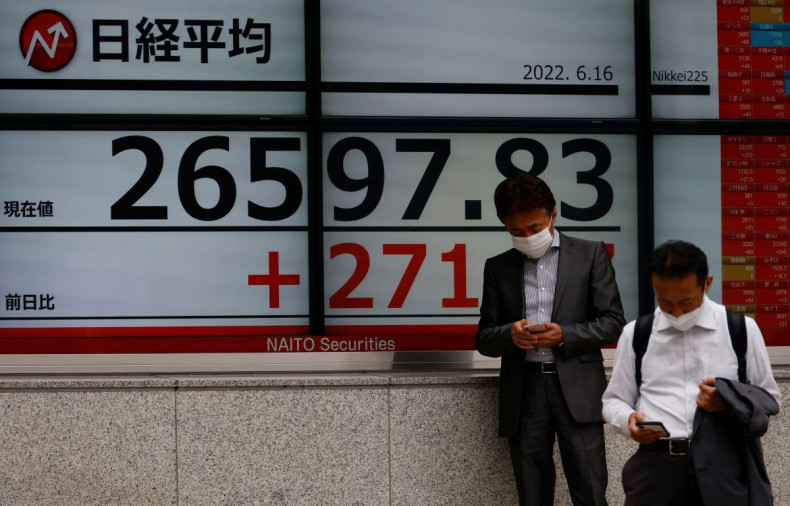 Men wearing protective masks amid the coronavirus disease (COVID-19) outbreak, use mobile phones in front of an electronic board displaying Japan's Nikkei index outside a brokerage in Tokyo, Japan June 16, 2022. 