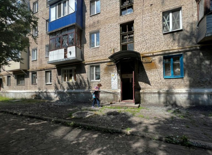 A woman cleans debris in front of a damaged residential building in Sloviansk, whose mayor accused Russia of waging war on civilians