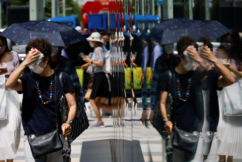 A woman wiping her face is reflected on a window while she walks on a street, as the Japanese government issues a warning over a possible power crunch due to a heatwave in Tokyo, Japan June 28, 2022.  