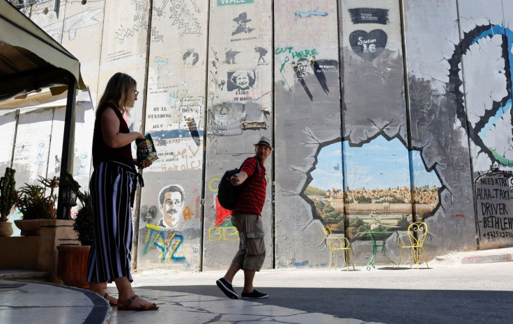 German tourists talk in front of a graffiti on the Israeli wall in Bethlehem, in the Israeli-occupied West Bank June 20, 2022. Picture taken June 20, 2022. REUTERSMussa Qawasma