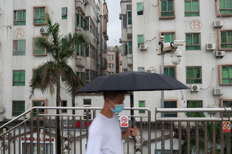 A man holding an umbrella walks on a pedestrian bridge by surveillance cameras, near Caopu in Shenzhen's Luohu district, Guangdong province, China July 5, 2022. 