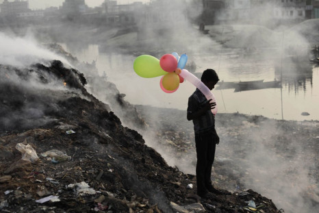 A boy plays with balloons by Buriganga river as smoke emits from a dump yard during sunset in Dhaka January 19, 2013. 