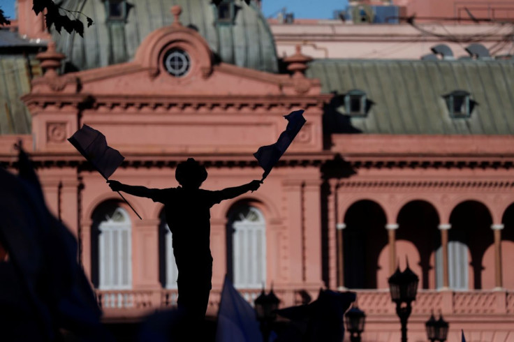 A person holding Argentine flags is silhouetted in front of the Casa Rosada presidential palace as farmers protest new export taxes on farm goods applied by President Alberto Fernandez's administration, in Buenos Aires, Argentina April 23, 2022.