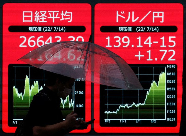 A man holding an umbrella is silhouetted as he walks in front of an electric monitor displaying the Japanese yen exchange rate against the U.S. dollar  and Nikkei share average in Tokyo, Japan July 14, 2022  