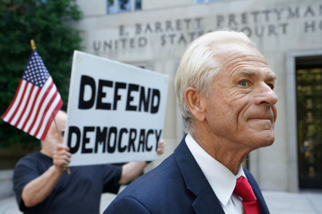 A protester holds a sign up behind Peter Navarro, adviser to former U.S. President Donald Trump, after Navarro's arraignment on contempt of Congress charges for refusing to cooperate with the House of Representatives committee investigating the January 6,