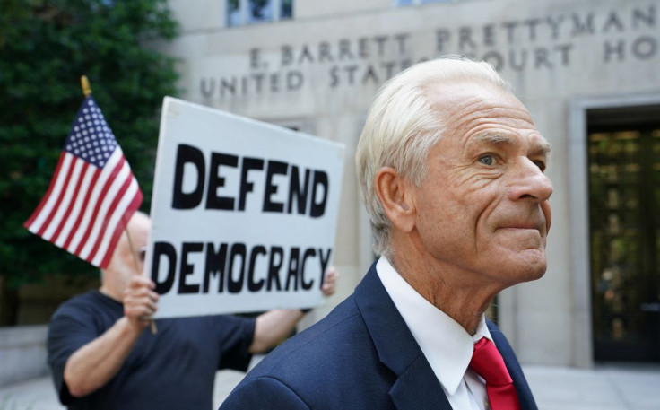A protester holds a sign up behind Peter Navarro, adviser to former U.S. President Donald Trump, after Navarro's arraignment on contempt of Congress charges for refusing to cooperate with the House of Representatives committee investigating the January 6,