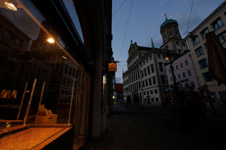 People sit near the unlit town hall, in Augsburg, Germany, July 21, 2022. The southern German municipality of Augsburg pledges to save energy by not illuminating touristic sites at night, warming public swimming pools or overheating public buildings 