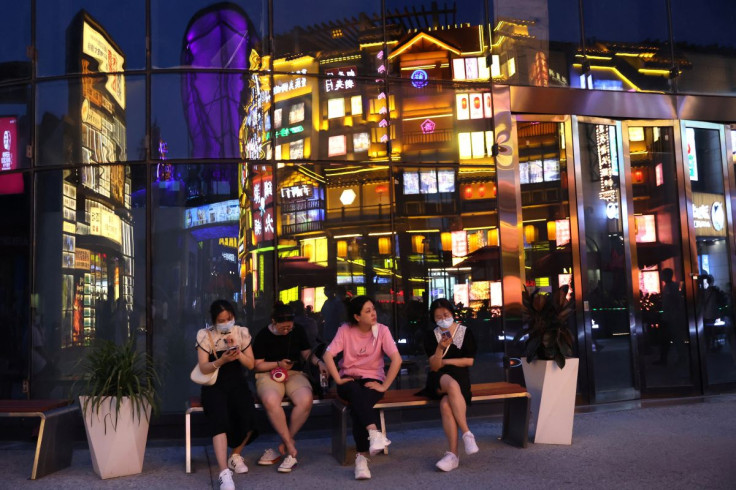 People sit near a building reflecting a restaurant, at a shopping area in Beijing, China July 25, 2022.