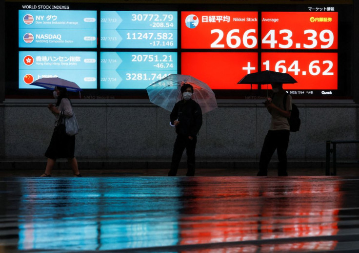 Passersby wearing protective face masks walk in front of an electronic board showing Japan's Nikkei share average, amid the coronavirus disease (COVID-19) pandemic, in Tokyo, Japan July 14, 2022. 