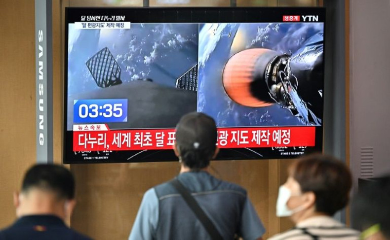 People in a railway station in Seoul watch a television screen showing a SpaceX Falcon 9 rocket launching with South Korea's first lunar orbiter Danuri onboard from Cape Canaveral in Florida