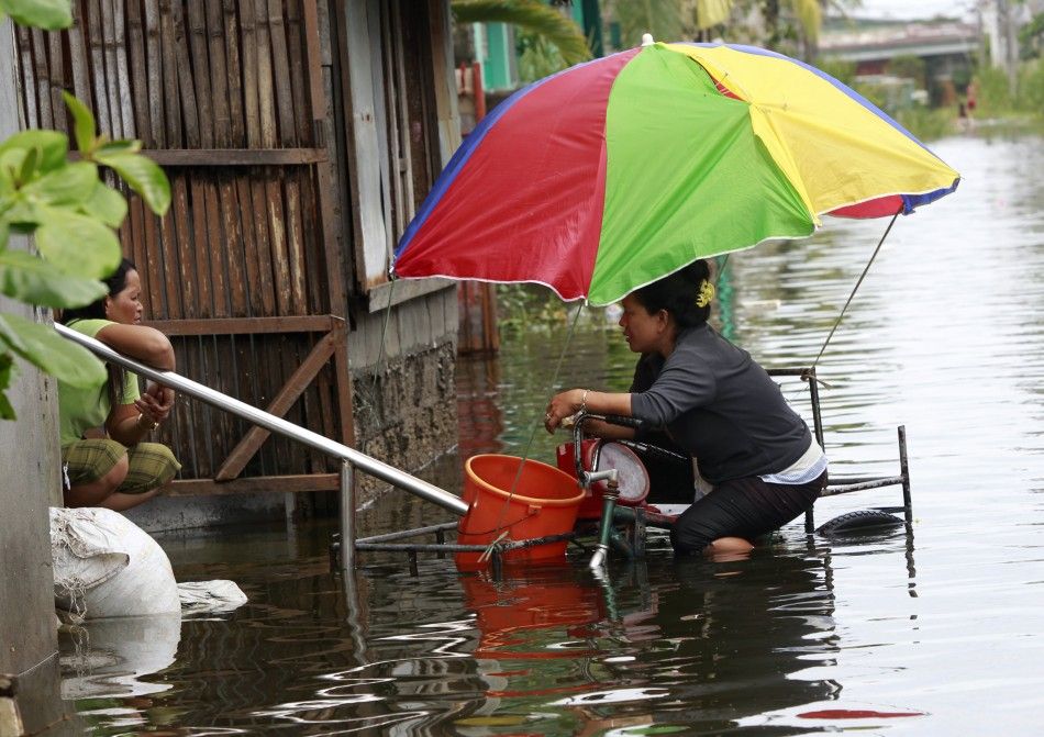 A woman in a pedicab half-submerged in floodwaters talks to a resident as she sells food in a residential area in Malabon