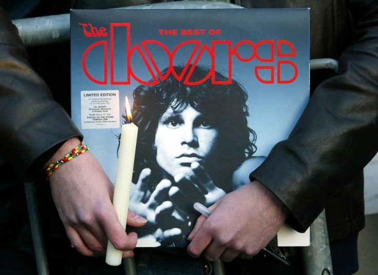 A fan holds an album by the seventies rock group The Doors and a candle near the tomb of late singer..