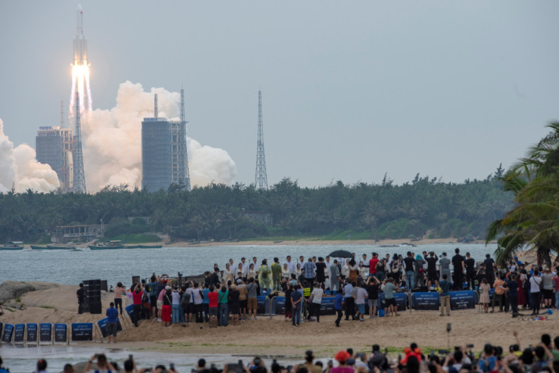 People watch from a beach as the Long March-5B Y2 rocket, carrying the core module of China's space station Tianhe, takes off from Wenchang