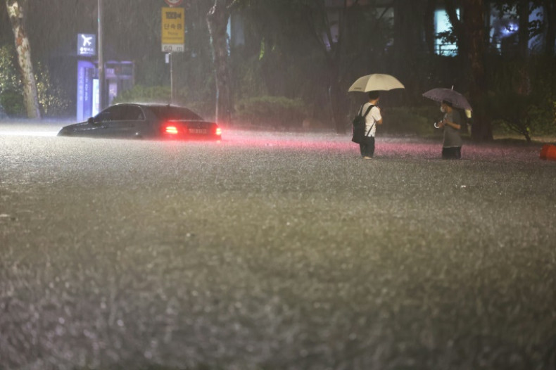 People wade alongside cars under water during heavy rainfall in Seoul's Gangnam district on Monday