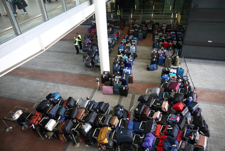 Airport workers stand next to lines of passenger luggage arranged outside Terminal 2 at Heathrow Airport in London